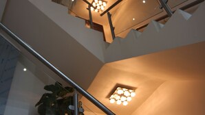 Ein mehrgeschossiges Interieur mit Treppe, Glasgeländern und Deckenleuchten.