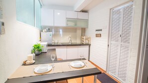 A compact kitchen with white cabinets, a microwave, and a sink. There is a dining table set with plates, cutlery, and a glass. - Garden Of Eden Houses (George Town)