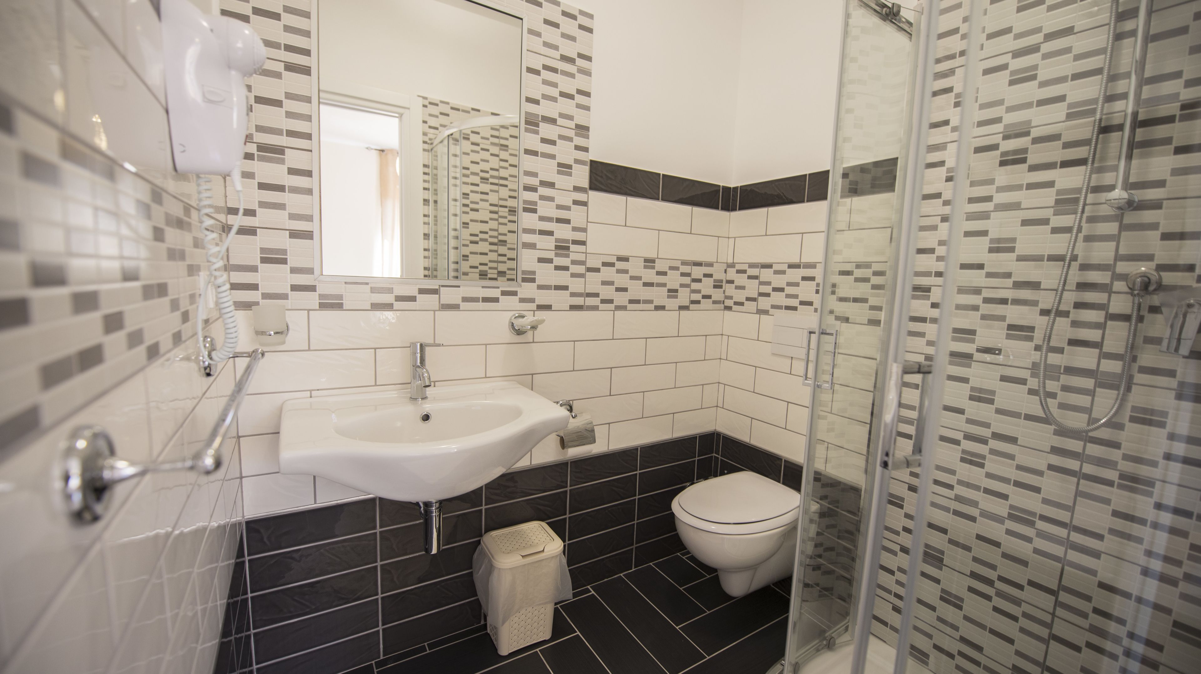 A modern bathroom with a white sink, black and white tiled walls, a glass shower enclosure, and a toilet.