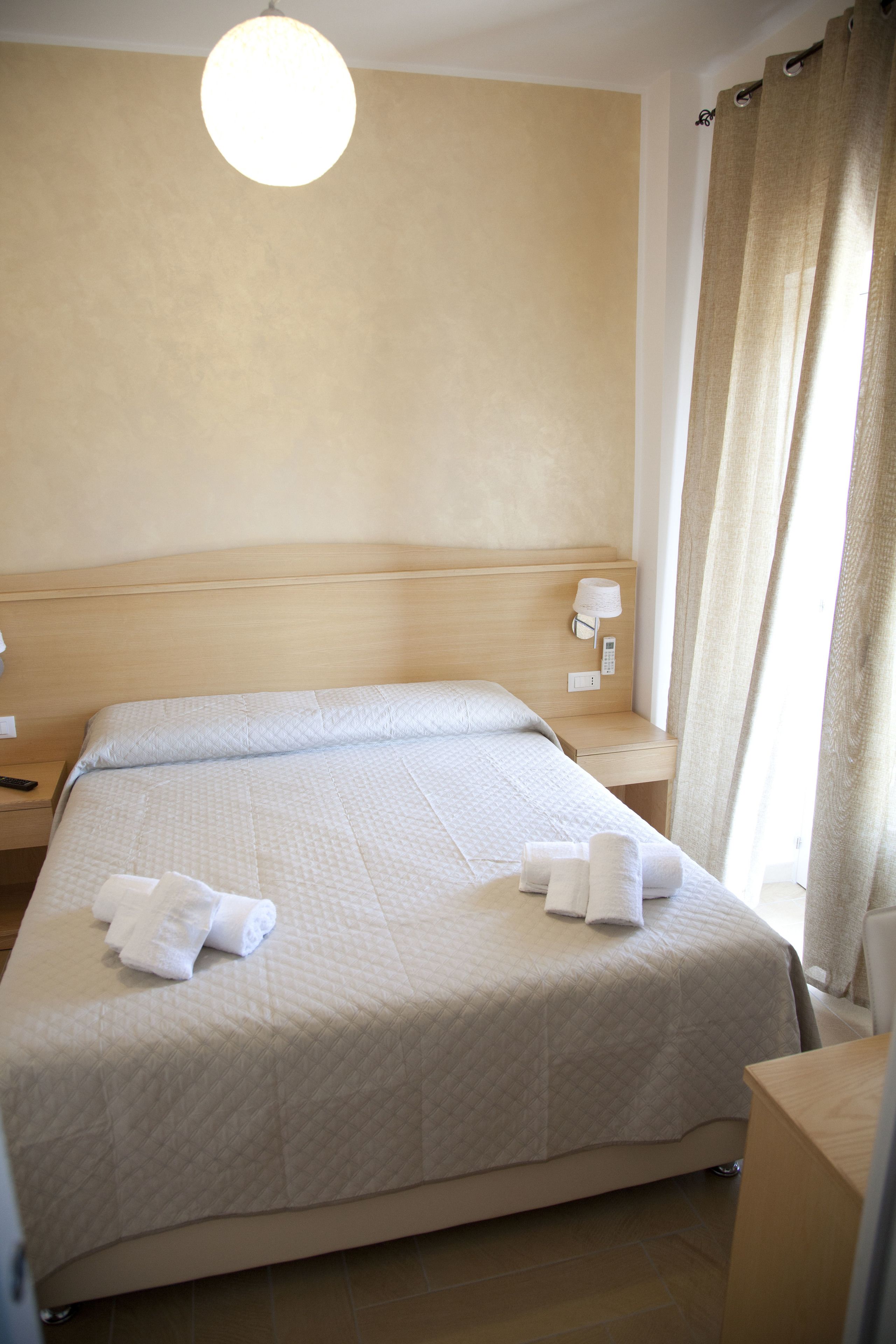 Una habitación de hotel con una cama grande, una mesita de noche y una lámpara, además de una cortina.