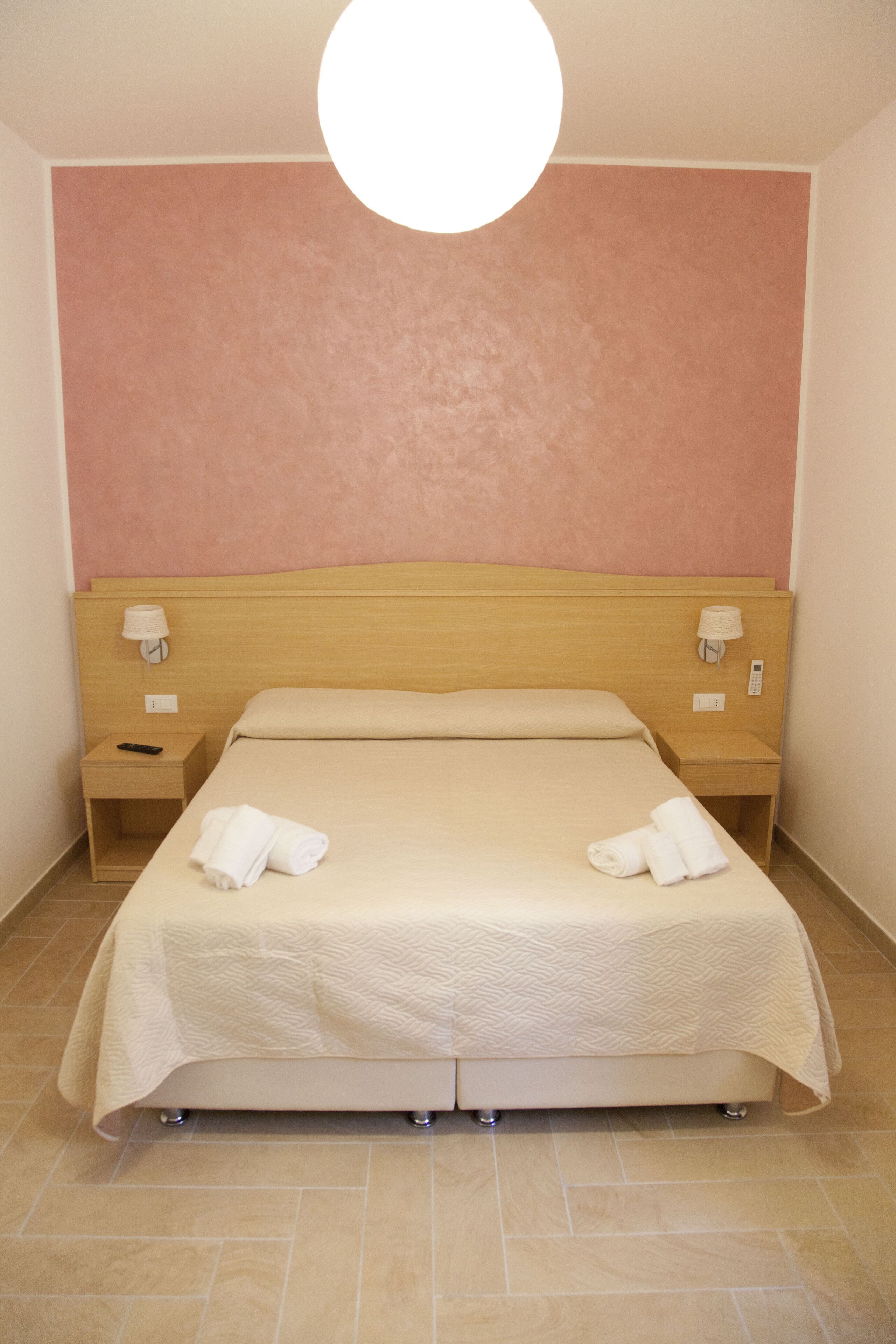 A neatly made bed with a headboard, two bedside tables with lamps, and a plain wall with a textured finish.