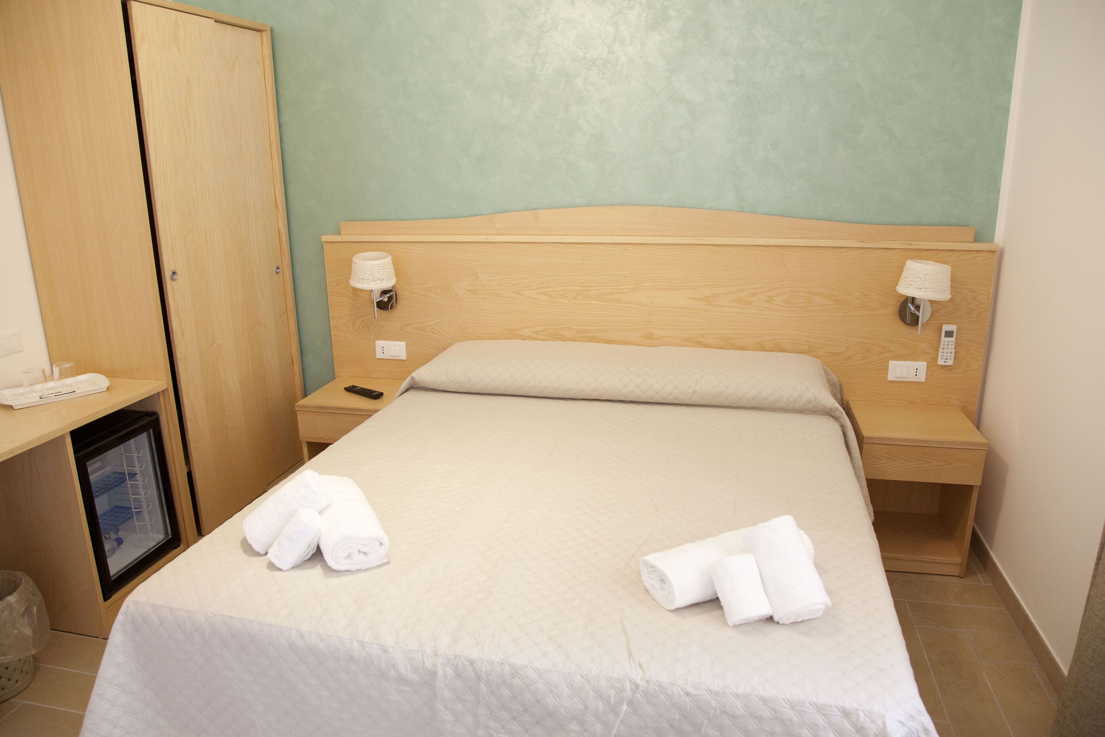 A hotel room with a bed, wooden headboard, two bedside tables with lamps, a small wooden cabinet, and a desk with a telephone.