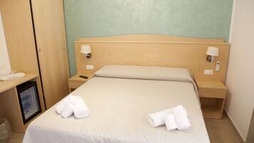 A hotel room with a bed, wooden headboard, two bedside tables with lamps, a small wooden cabinet, and a desk with a telephone.