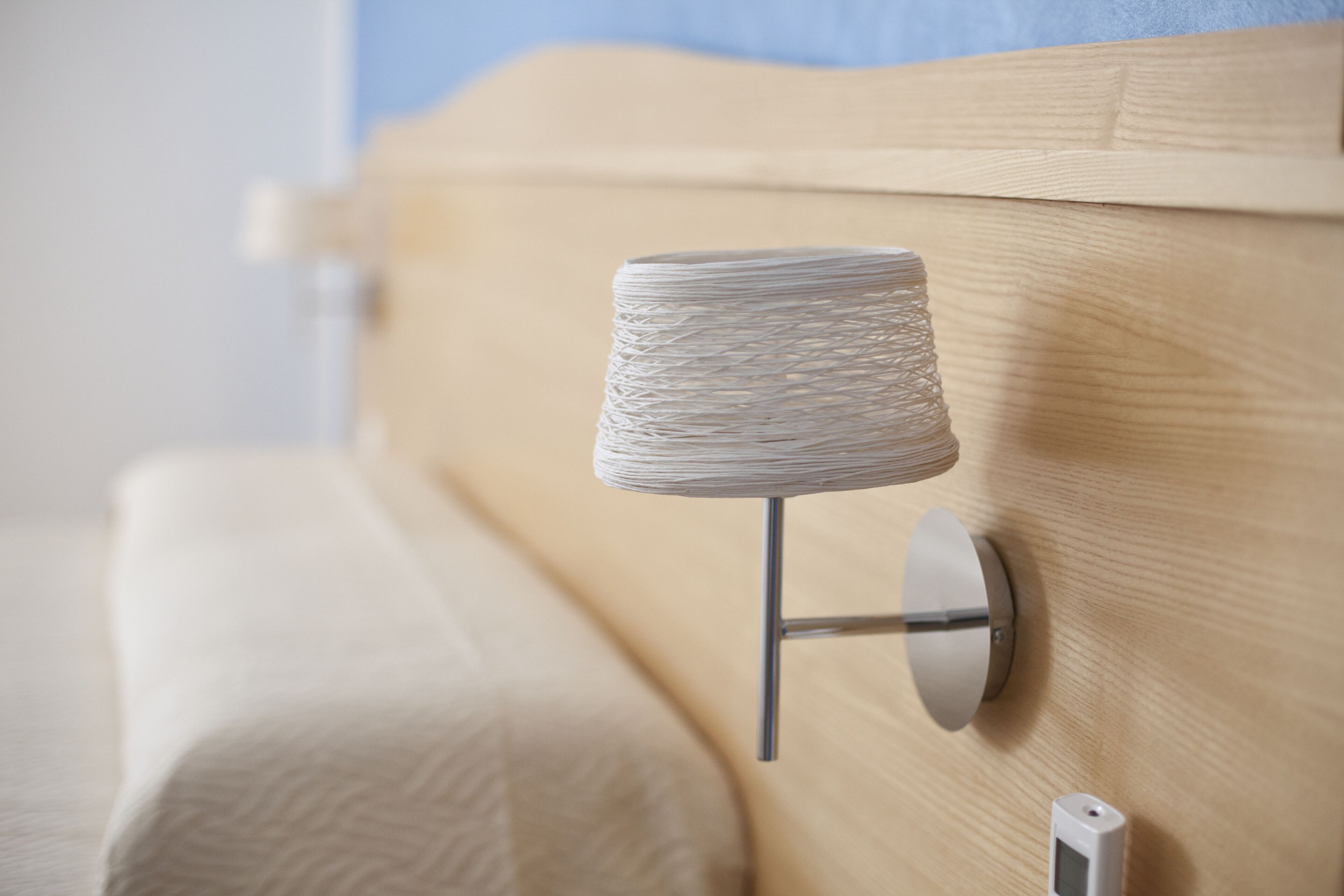 A modern lamp with a textured shade mounted on a wooden headboard.