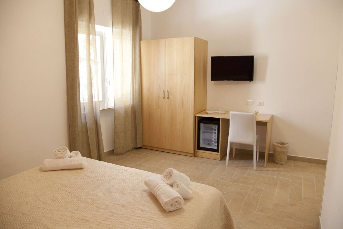 Hotellihuone, jossa on sänky, työpöytä, tuoli, vaatekaappi ja televisio.