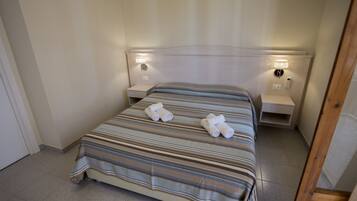 A neatly made bed with striped bedding and two rolled towels on it. There are bedside tables with lamps on either side of the bed.