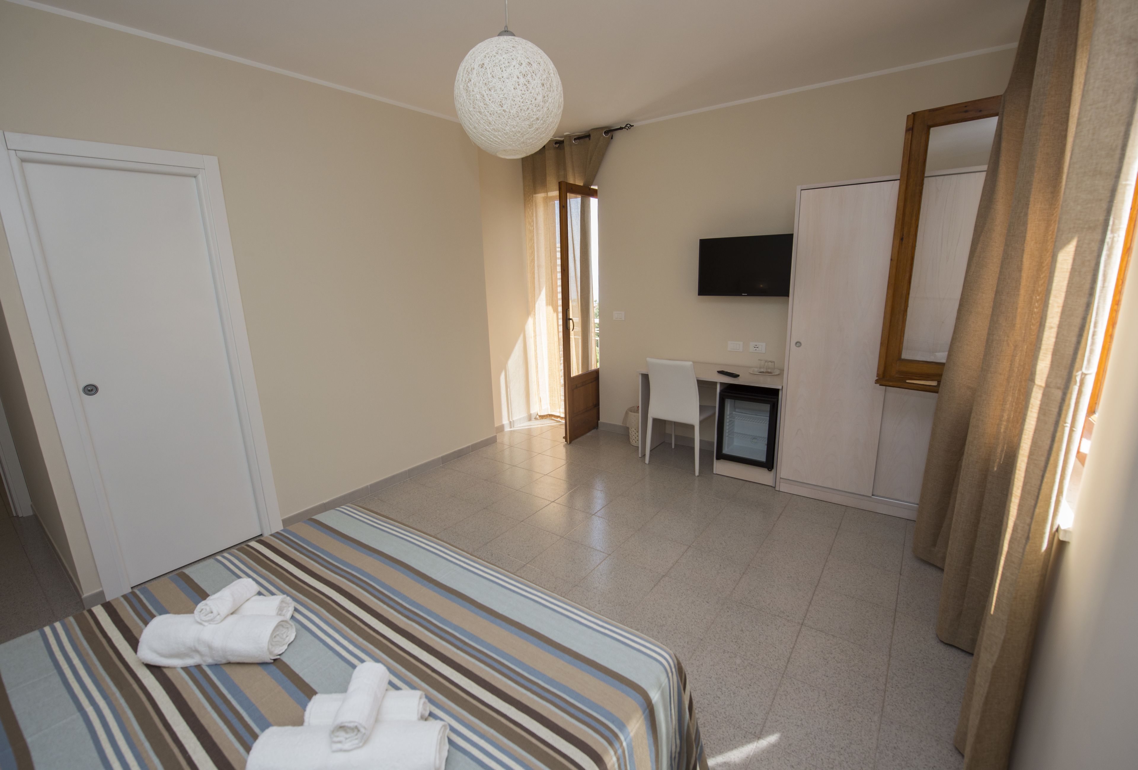 Una habitación de hotel con cama, escritorio, televisor y espejo.