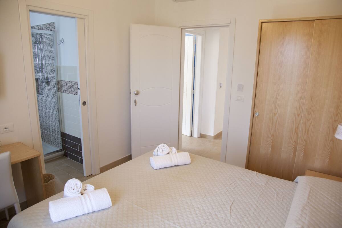 Hotellihuone, jossa on sänky, puuovi, suihkulla varustettu kylpyhuone ja peili.