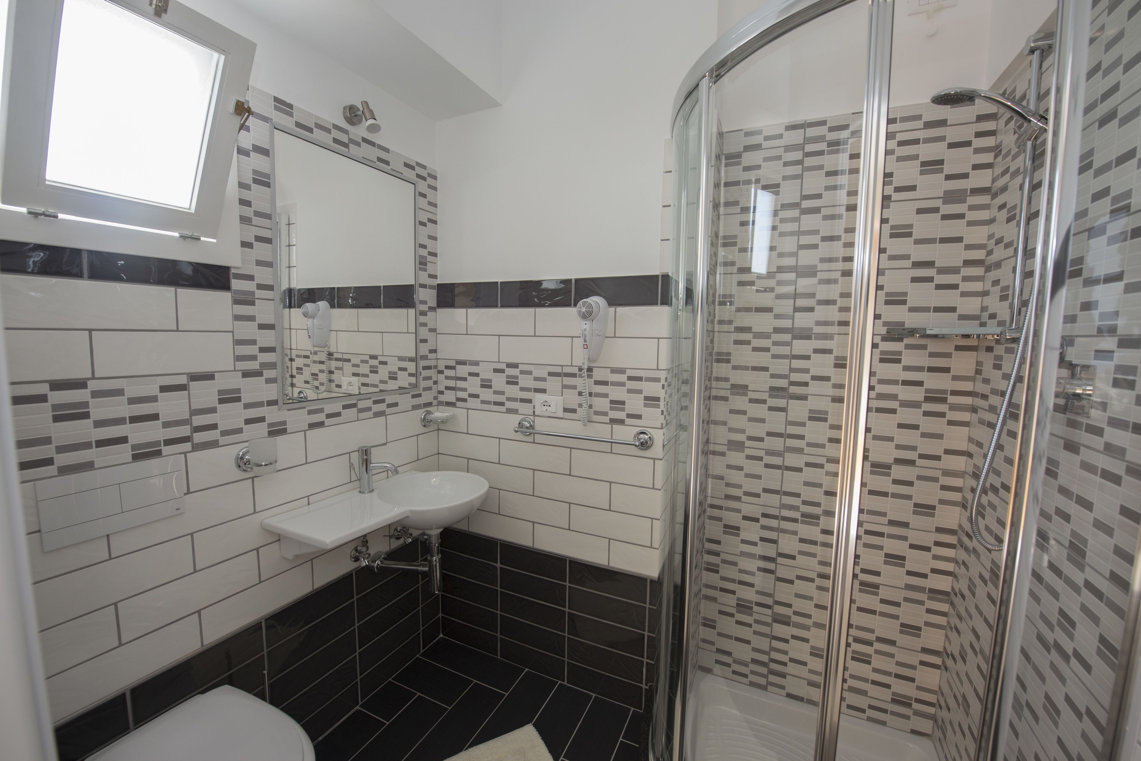 Een moderne badkamer met een douche met glazen wand, een witte wastafel en een betegelde vloer.