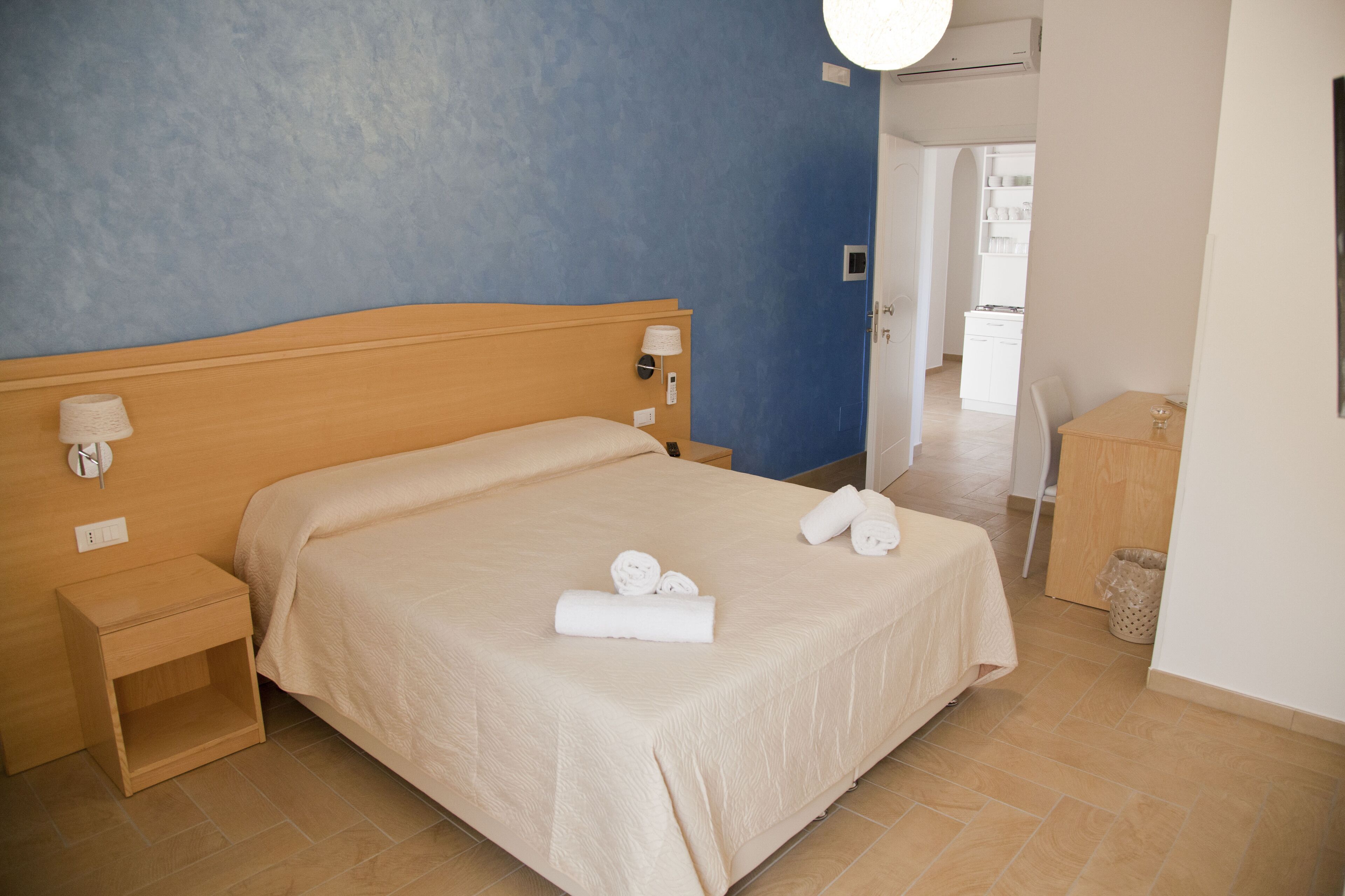 A hotel room with a bed, bedside tables, a lamp, and a view of the hallway.