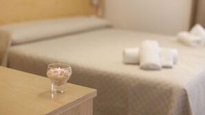 Een hotelkamer met een netjes opgemaakt bed, een nachtkastje met een kaars, en handdoeken op het bed.