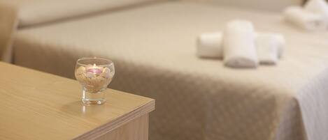 A hotel room with a neatly made bed, a bedside table with a candle, and towels on the bed.