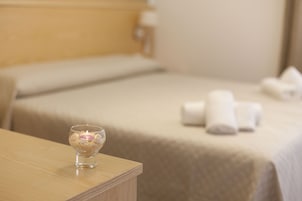 Habitación de hotel con una cama bien hecha, una mesita de noche con una vela y toallas sobre la cama.