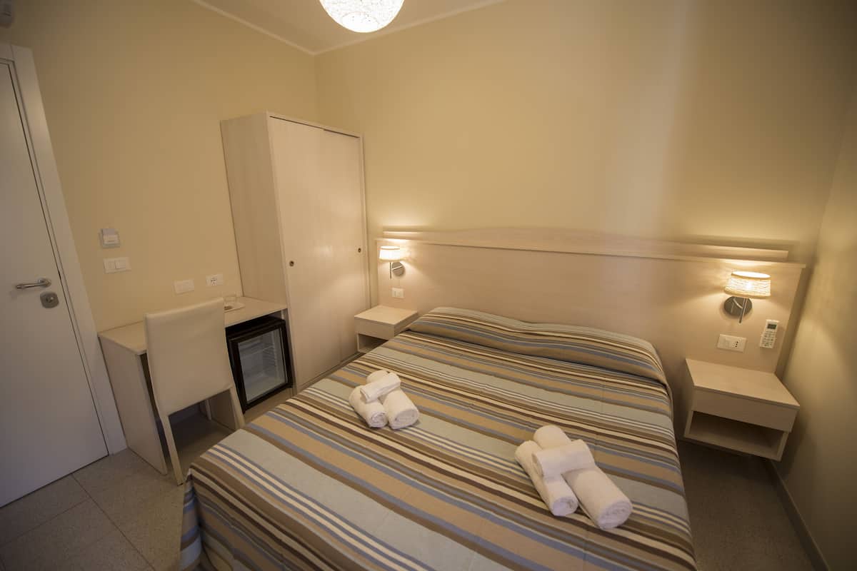 Hotellihuone, jossa on sänky, työpöytä, vaatekaappi ja televisio.