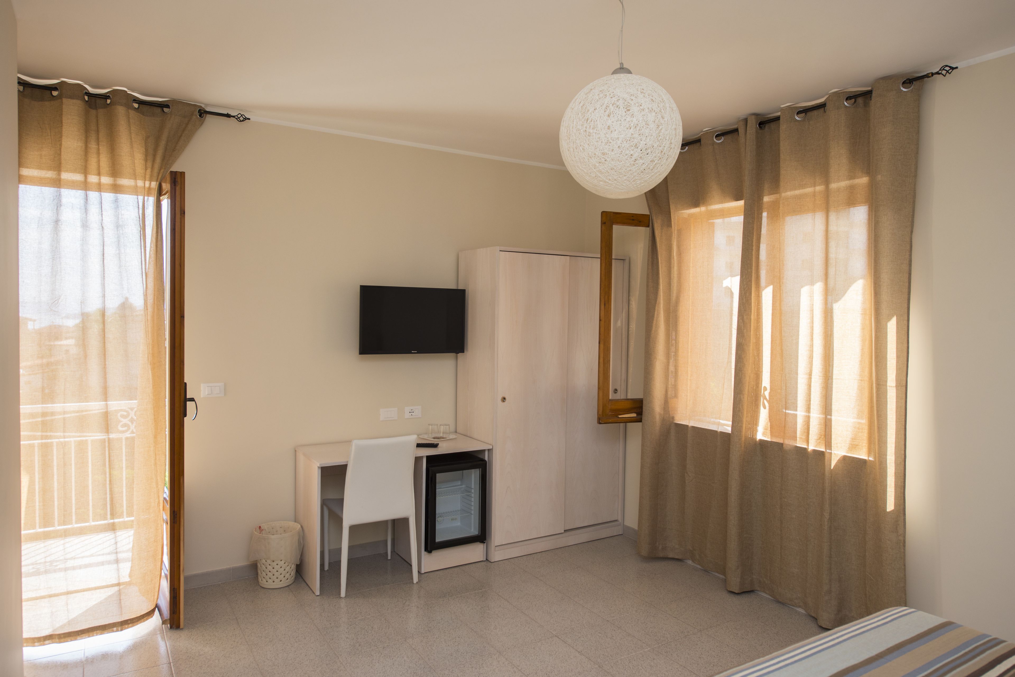 A room with a desk, a television, a wardrobe, and a small refrigerator.