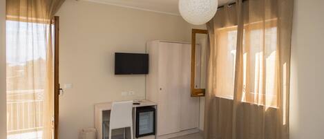 A room with a desk, a television, a wardrobe, and a small refrigerator.