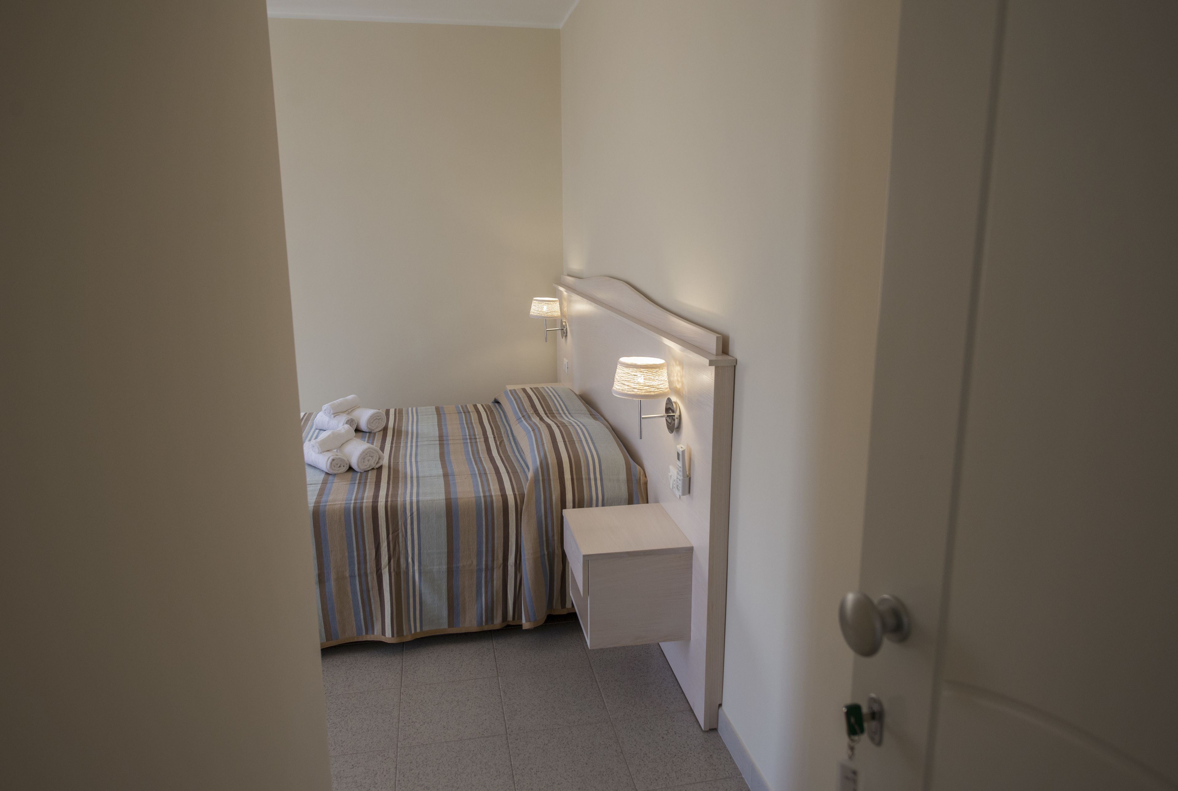 A small, neatly arranged bedroom with a bed, bedside lamps, and a nightstand.