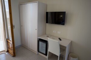 Habitación compacta con escritorio blanco, refrigerador pequeño, televisión montada en la pared y armario.