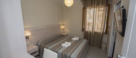 Una habitación de hotel con cama, mesitas de noche, un escritorio, televisión y cortinas.