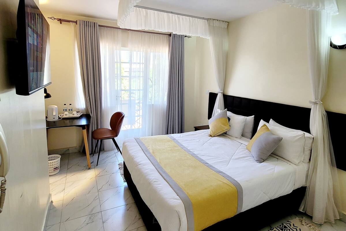 A hotel room with a large bed, a desk with a chair, a television, and a patterned rug.