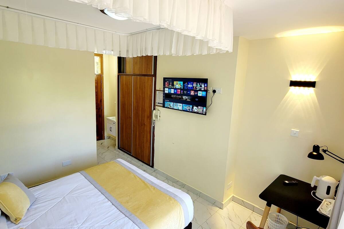 A bedroom with a bed, bedside table, chair, and a TV mounted on the wall.