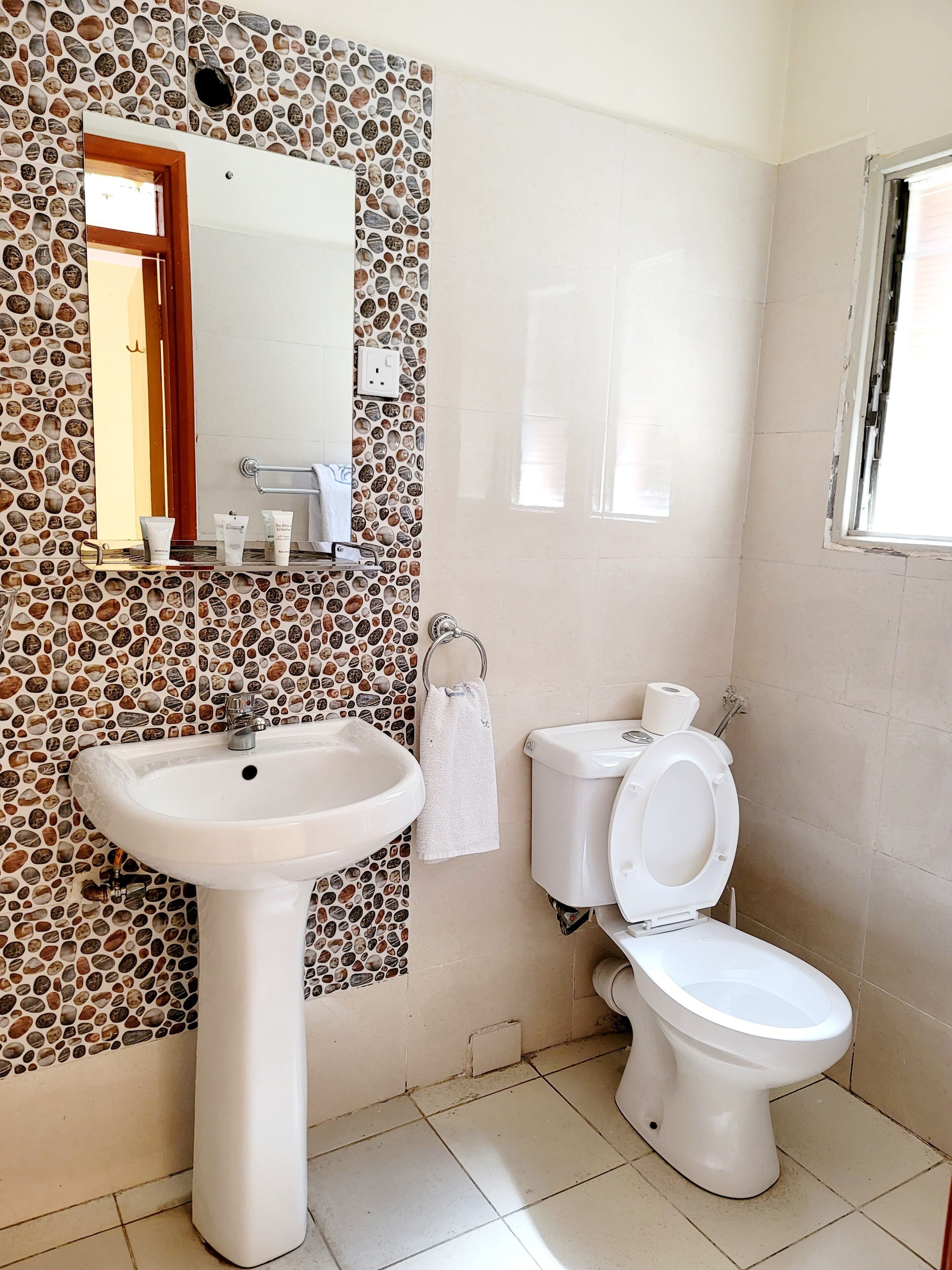 A bathroom with a stone mosaic backsplash, a white sink, a toilet, and a mirror.