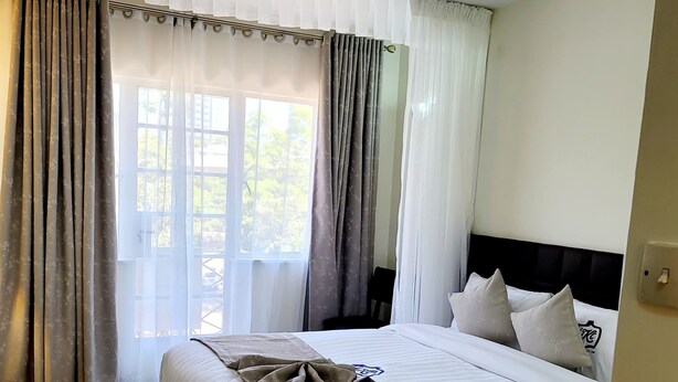 A hotel room with a large bed, a ceiling light, and a window with curtains. - United Kenya Club (Nairobi)