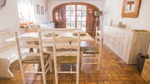 A dining area with a wooden table and white chairs, a kitchen with a wooden cabinet, and a large arched window.