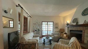 A cozy living room with a fireplace, a television, and a large window with curtains.