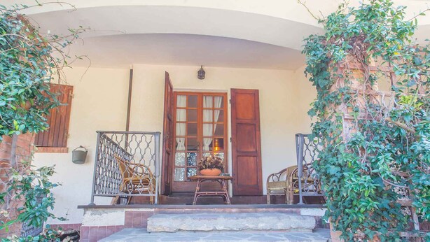 A covered porch with a wooden door, a small table with chairs, and a stone staircase leading up to the door.