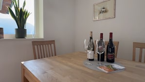Mesa de jantar com três garrafas de vinho e copos, um vaso de planta e um quadro na parede.