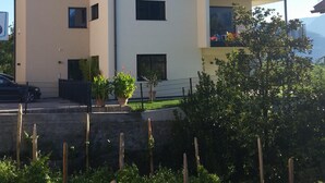 Um edifício de dois andares com varanda no andar superior, rodeado por vegetação.