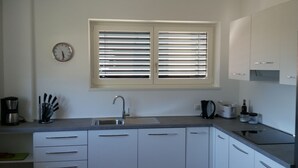 Uma cozinha moderna com armários brancos, uma pia de aço inoxidável e uma janela com persianas.