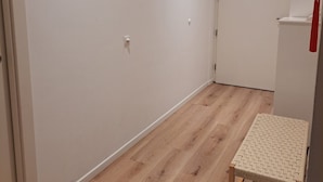 Um corredor com piso de madeira, um banquinho tecido pequeno e três quadros na parede.