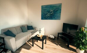 A living room with a sofa, a coffee table, a TV, and a painting on the wall.