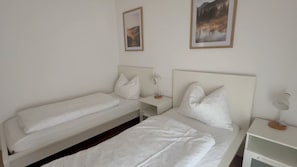A twin room with two beds, a bedside table, a nightstand, and two wall-mounted pictures.