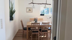A dining area with a wooden table, four chairs, two wine bottles, and two wine glasses.