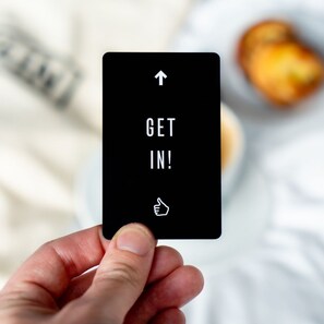 A hand holding a playing card with the text "GET IN!" and a thumbs-up icon.