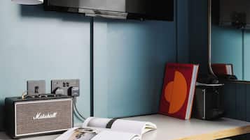 Una habitación moderna con una televisión de pantalla plana, un amplificador Marshall, un refrigerador Smeg, un taburete y un libro titulado 'Verner Panton'.
