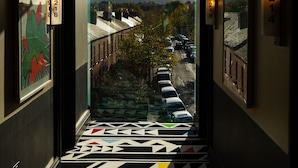 A modern hotel hallway with a geometric patterned floor, glass railings, and a view of a cityscape.