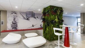 Ett modernt loungeområde med en väggmålning som föreställer klassiska flygplan, en grön vertikal trädgård och moderna vita möbler.