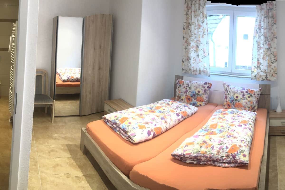 A narrow room with a bed, a window with curtains, and a door.