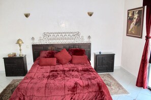 A bedroom with a large bed, two nightstands, a decorative headboard, and a painting on the wall.