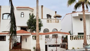 Un edificio blanco con techo de tejas rojas, varias ventanas y una entrada portonada.