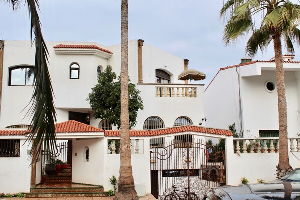 A white building with a red-tiled roof, multiple windows, and a gated entrance.
