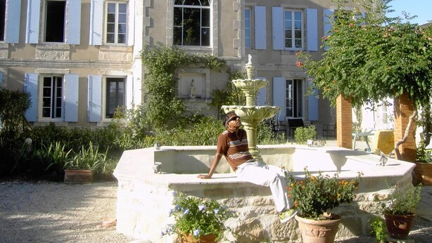Un edificio histórico con una fuente, una estatua y una persona sentada en un banco de piedra.