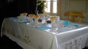 Una mesa dispuesta con cristalería transparente y servilletas azules, cubierta por un mantel blanco con bordados dorados.