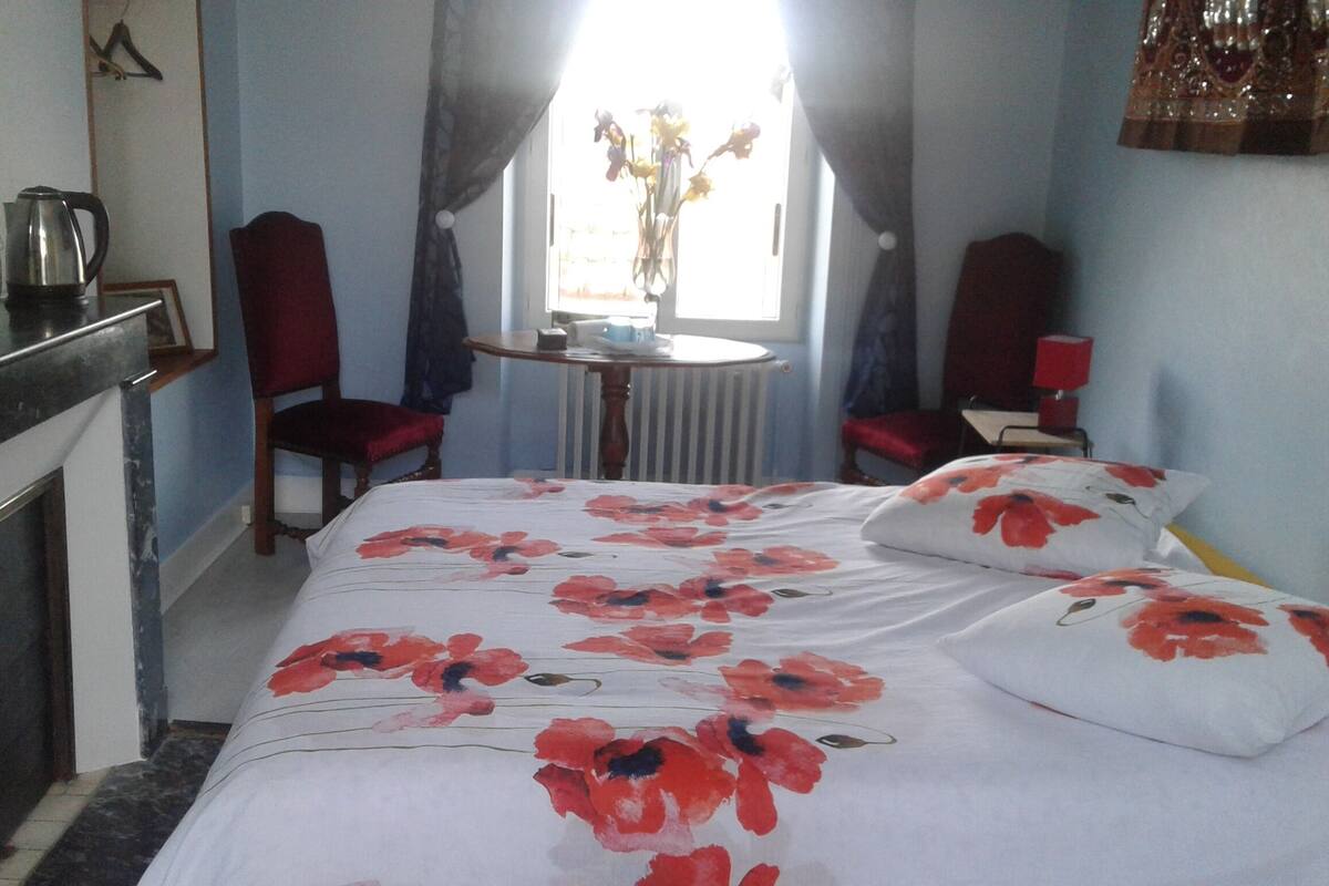 A bedroom with a bed, a chair, a table, and a radiator.
