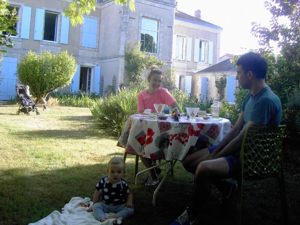 An outdoor dining area with a table set for two, surrounded by greenery and a building in the background.