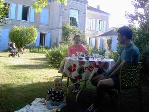 An outdoor dining area with a table set for two, surrounded by greenery and a building in the background. - L'Isle de Bourbon (Le Gue-de-Velluire)